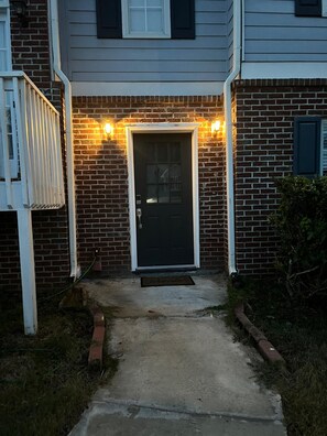 A residential entrance with a brick facade, a dark-colored door, and two wall-mounted lights. - Private 2BR Guest Suite, No Stairs, Garage (Woodstock)