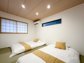 A room with two beds, a window with a view, and an air conditioning unit. - HANASTAY MUKAI HOTARU (Osaka)