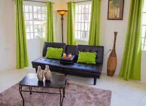 A living room with a black sofa, green cushions, a coffee table with vases, a floor lamp, and a large vase. - A welcoming light open concept two bedroom apartment. (San Juan)