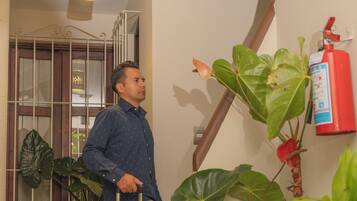 Una persona con una maleta en un pasillo con plantas en macetas y un extintor en la pared.