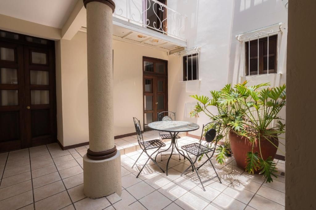 Un patio con una mesa redonda y sillas, una planta grande en maceta y una columna.