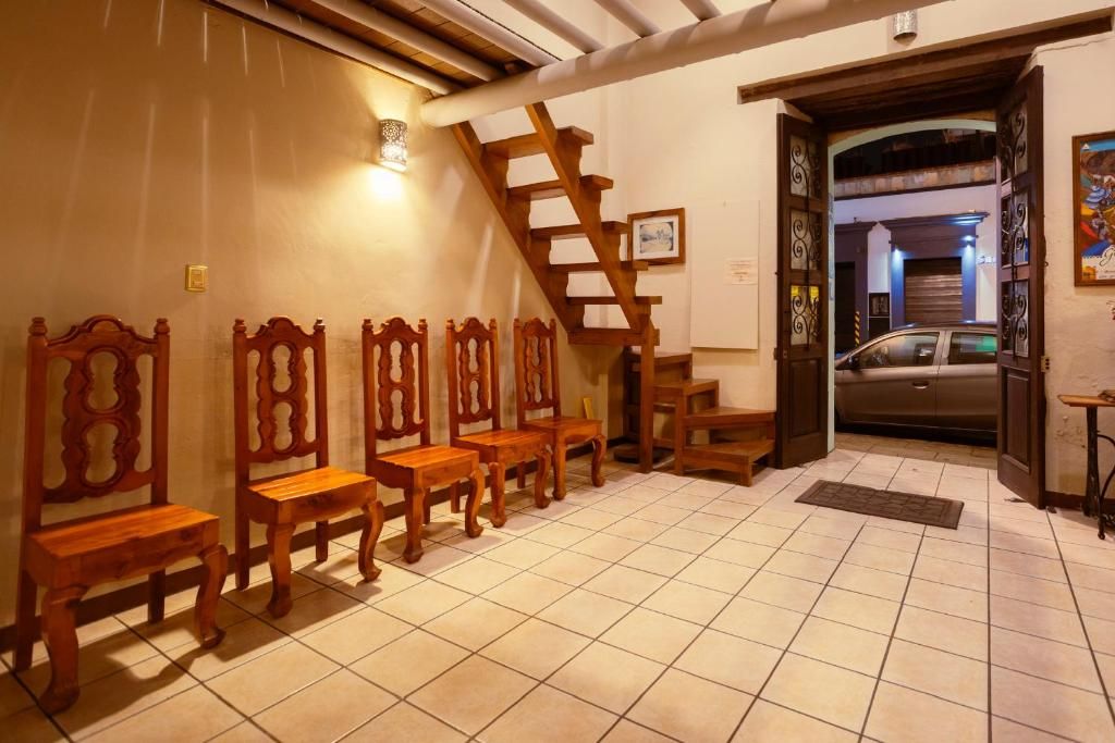 Una habitación con piso de baldosas, sillas de madera, una escalera de madera y un coche estacionado afuera.