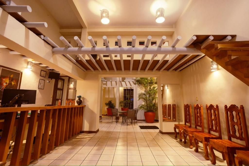 Un vestíbulo de hotel con suelo de baldosas, bancos de madera, un mostrador de recepción y una escalera.