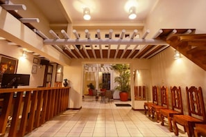 Un vestíbulo de hotel con suelo de baldosas, bancos de madera, un mostrador de recepción y una escalera.