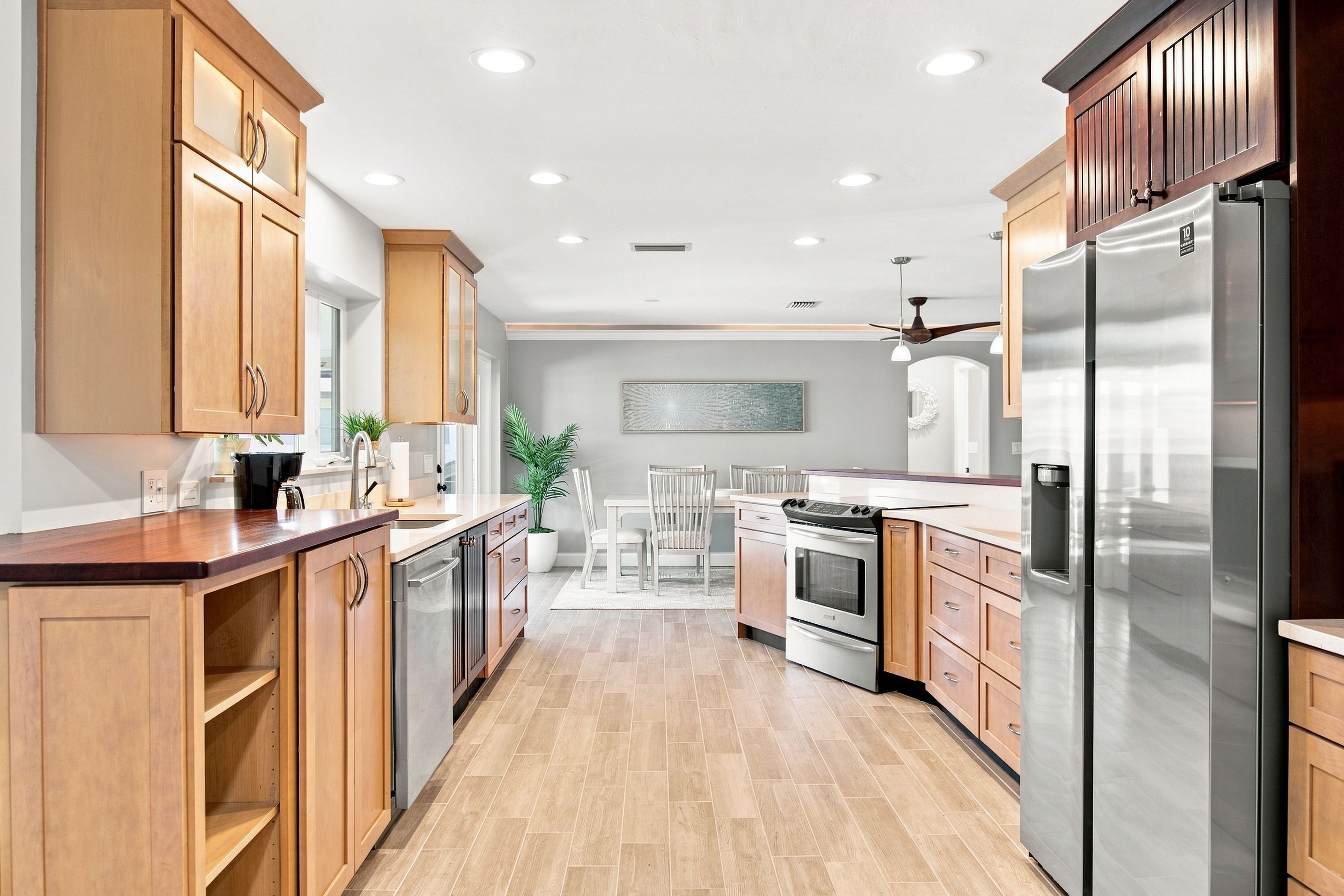 A modern kitchen with wooden cabinets, stainless steel appliances, and a dining area with a white table and chairs.