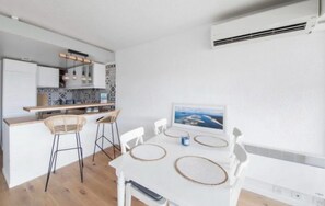 A modern kitchen with a dining area, featuring a white table with a picture, bar stools, and a built-in island. - Apartment next to the beach - 4P (Arcachon)