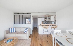 A compact living space with a kitchenette, a dining area with a white table and chairs, and a sofa with striped pillows. - Apartment next to the beach - 4P (Arcachon)