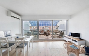 A spacious living room with a large sliding glass door leading to an outdoor area, a dining table with chairs, a sofa, and a TV on a stand. - Apartment next to the beach - 4P (Arcachon)