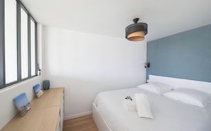 A bedroom with a bed, a bedside table, a lamp, and a window. - Apartment next to the beach - 4P (Arcachon)