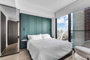A modern bedroom with a large bed, a nightstand, a teal accent wall, and a view of a cityscape through a large window. - E11EVEN Miami Double Vacation (Miami)