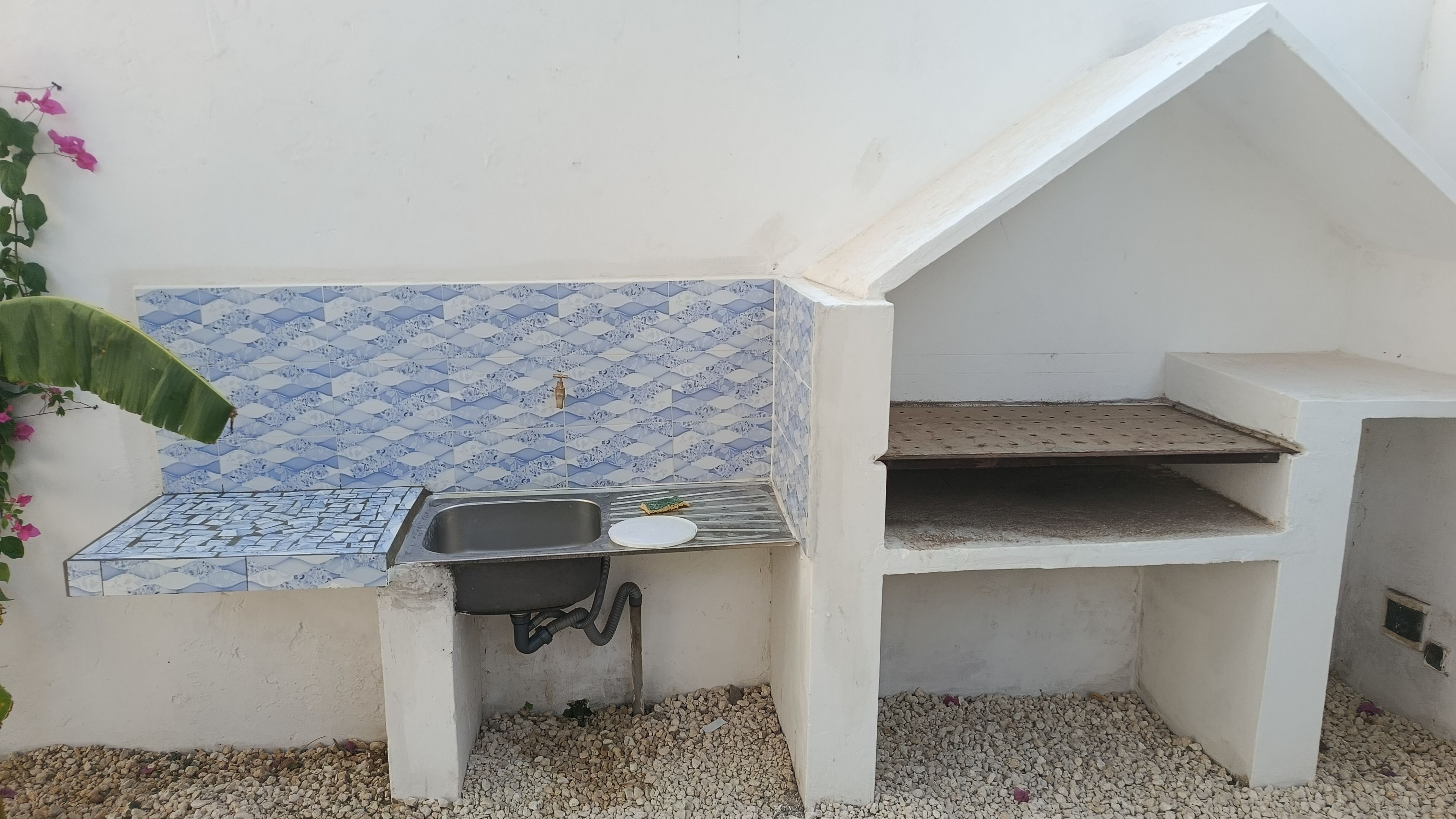 Una cuina exterior petita amb un rentaplat, un plat i un respatller de rajola.