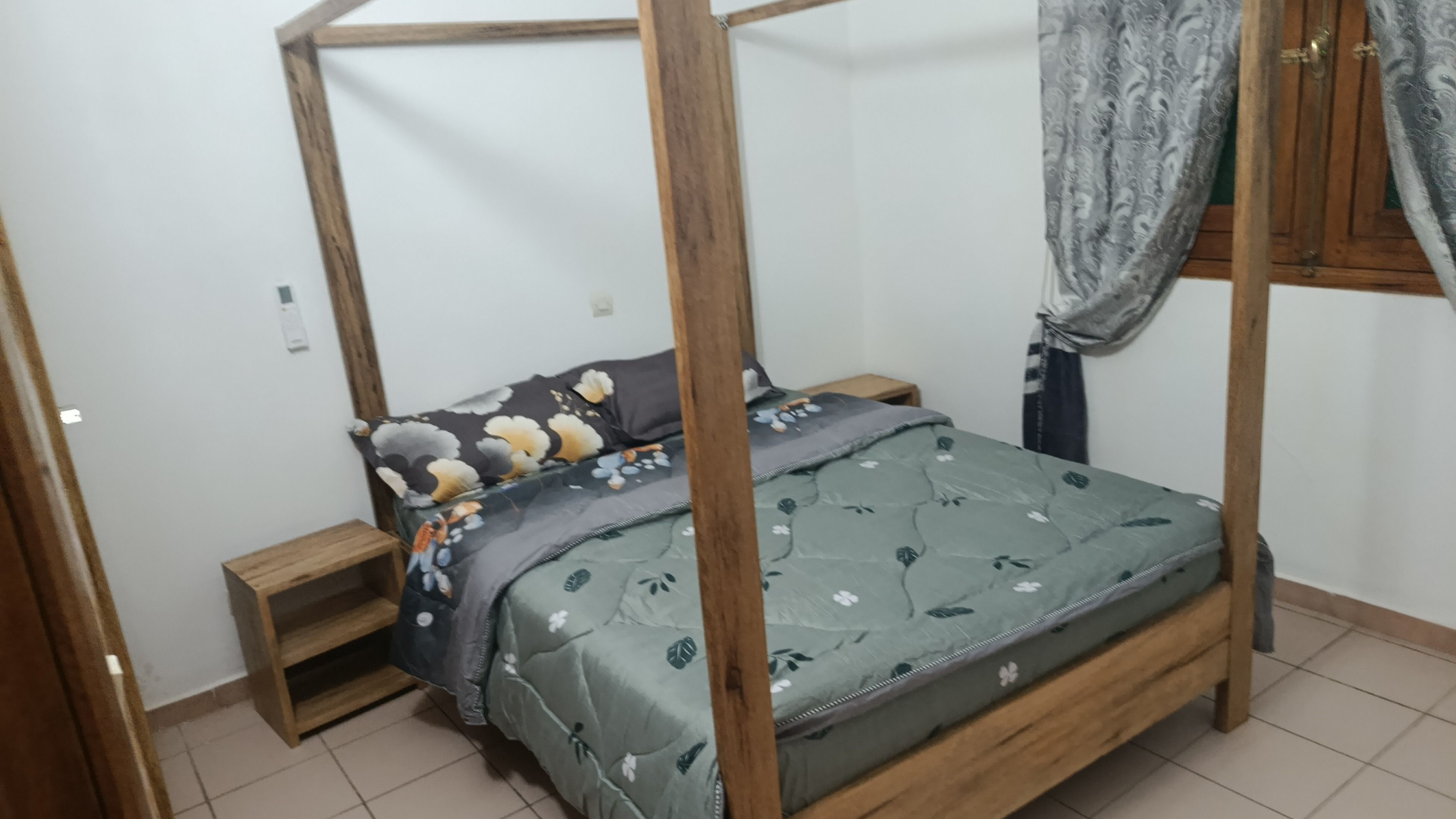 Een eenpersoonsbed met houten frame en hemel, een nachtkastje en een klein nachtkastje.
