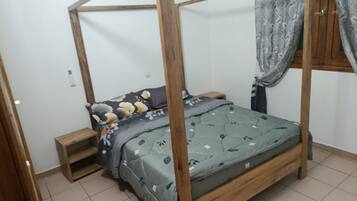 Een eenpersoonsbed met houten frame en hemel, een nachtkastje en een klein nachtkastje.