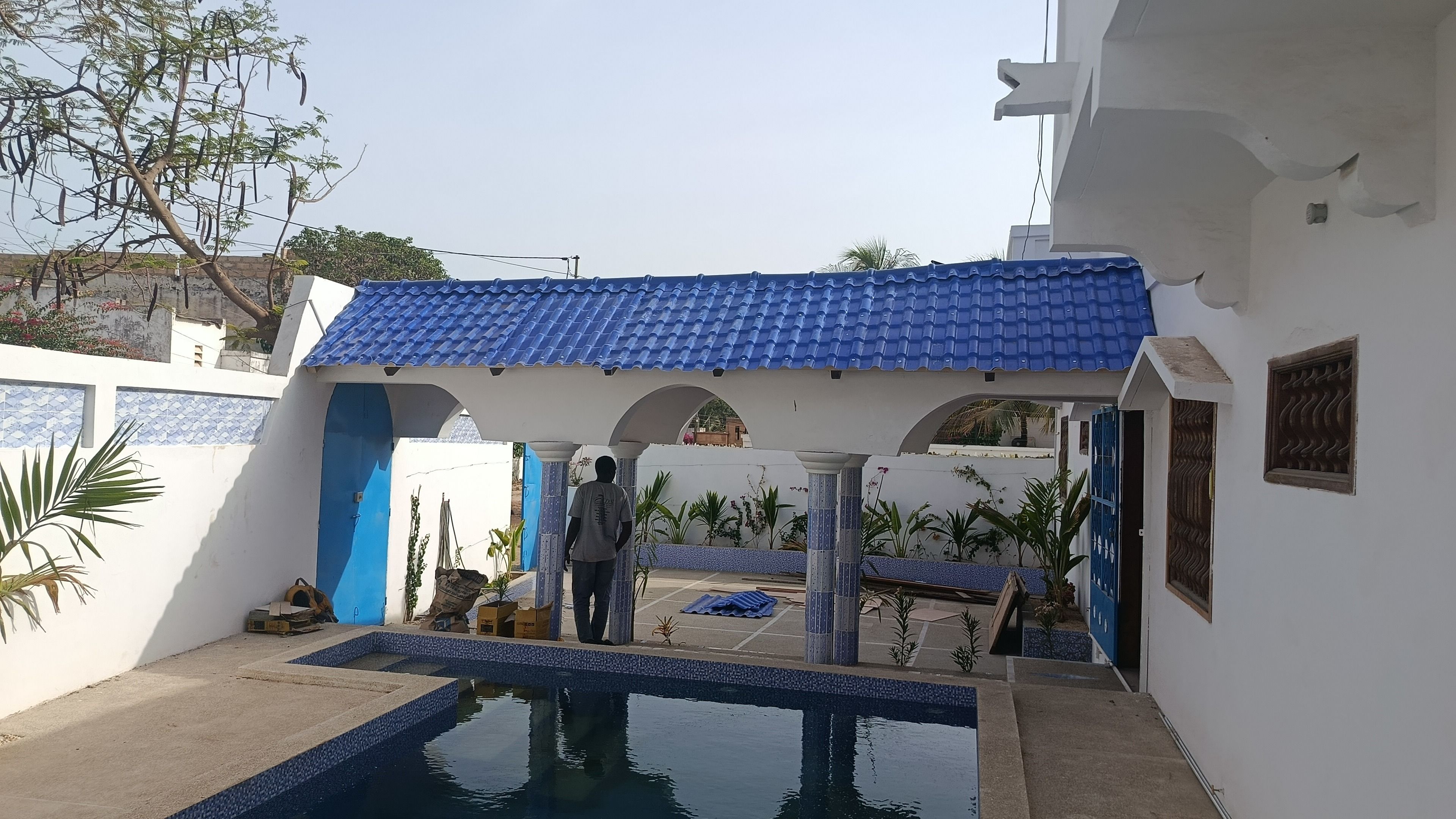 Un área de piscina con techo de azulejos azules, paredes blancas y cielo despejado.