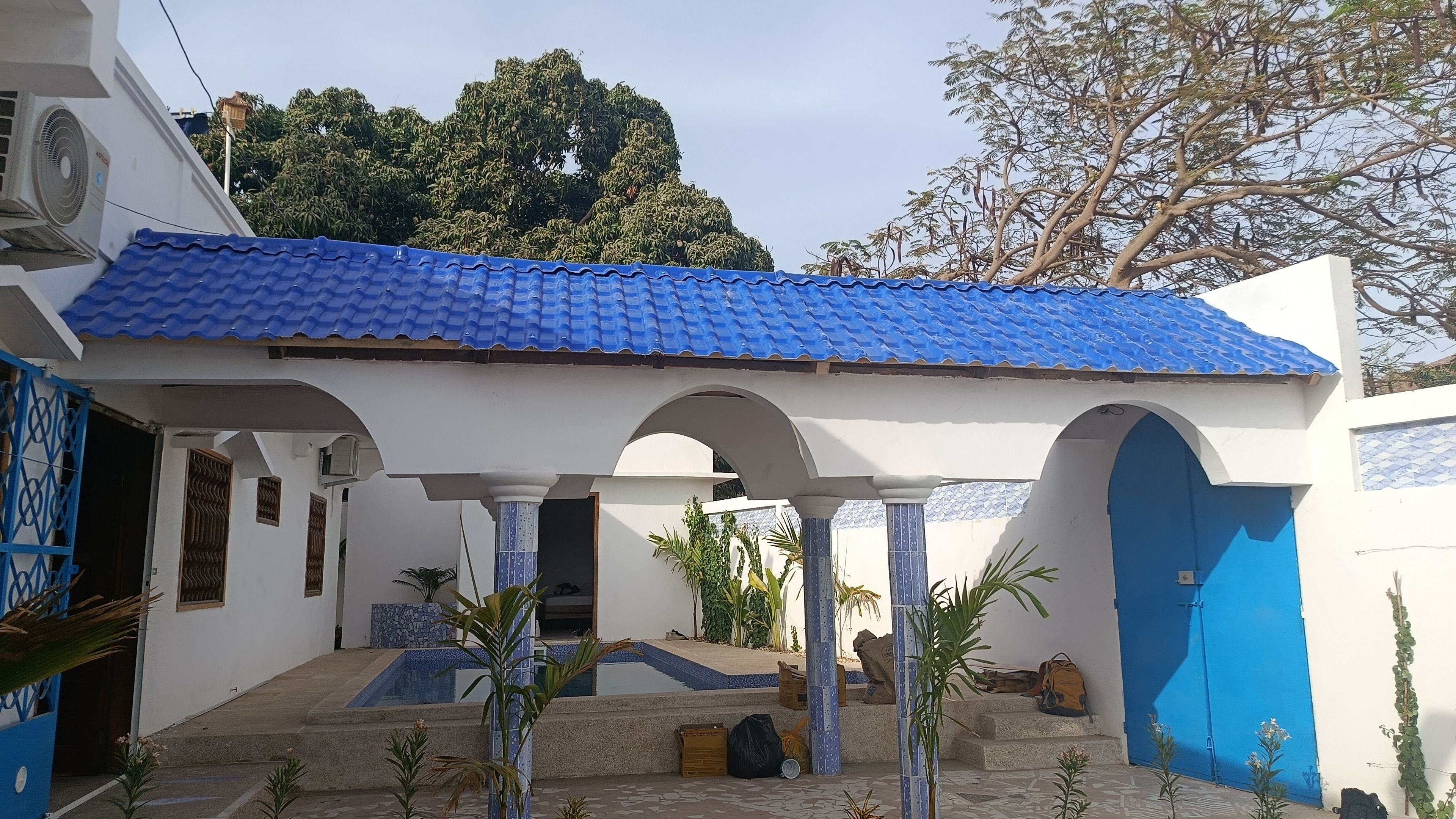 Un bâtiment doté d’un toit recouvert de tuiles bleues, de murs blancs et d’un patio abrité avec des colonnes.