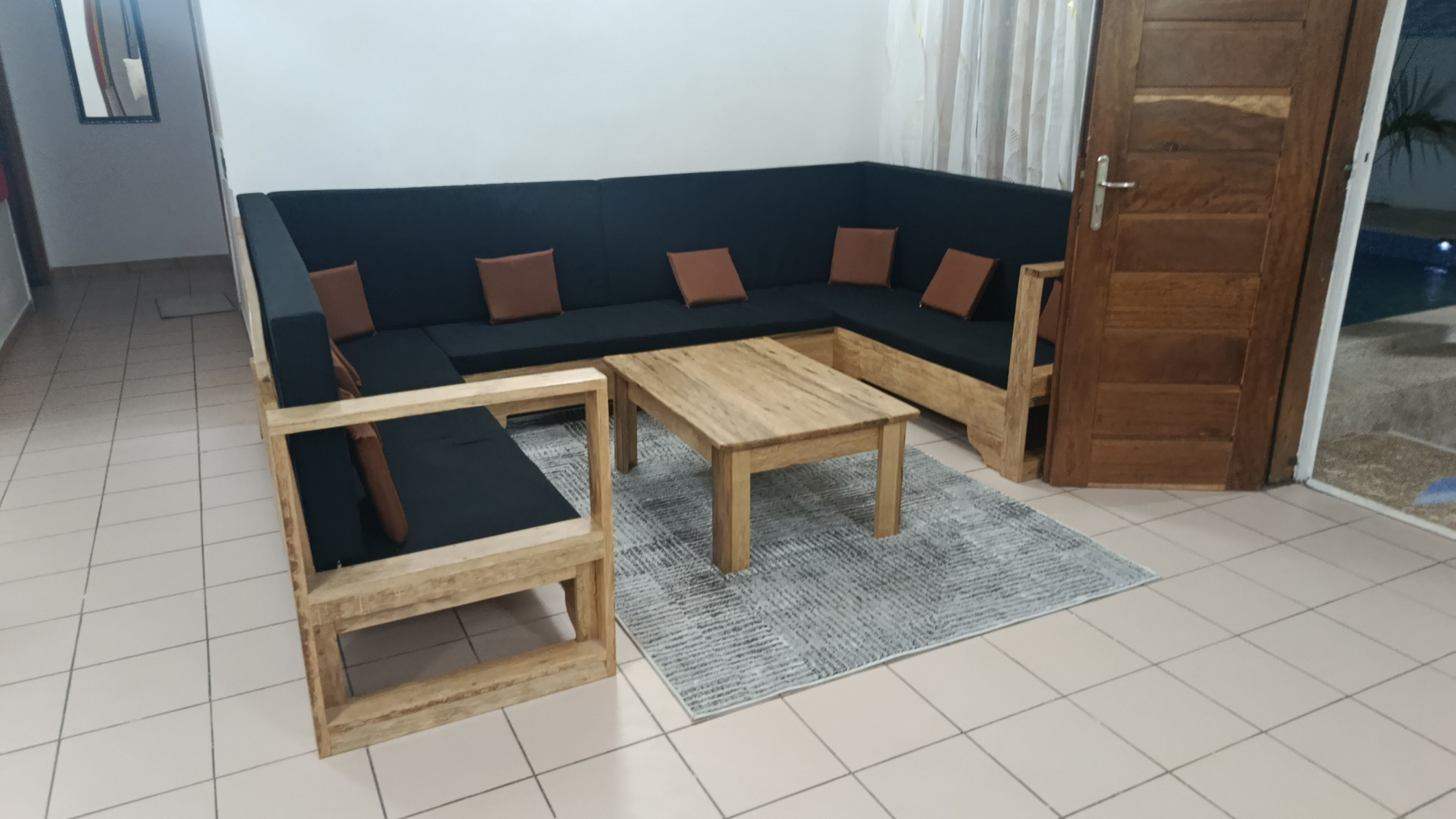 Un salon comprenant un canapé d’angle, deux tables en bois et un tapis à motifs.