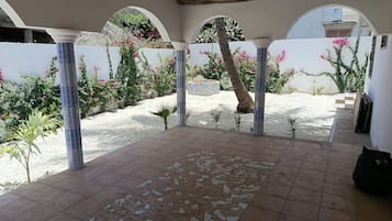 Un patio couvert doté d’un sol carrelé, de colonnes et d’un mur blanc orné de plantes à fleurs.
