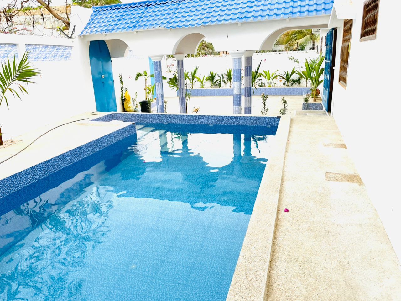Una piscina amb vora de rajola blava, envoltada per un edifici blanc amb detalls blaus i columnes.