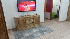 Ein Zimmer mit einem Holzkasten, einem an der Wand montierten Fernseher und einem gemusterten Teppich.