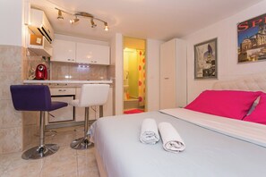 A hotel room with a bed, two chairs, a small kitchenette, and a bathroom visible through an open door. - Modern and practical studio apt in the heart of Split (Split)