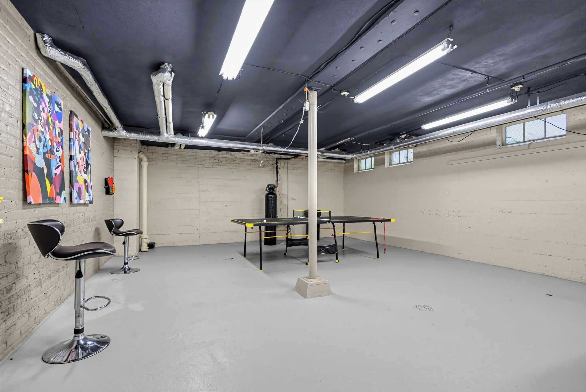 Une pièce avec une table de ping-pong, des chaises et des œuvres d’art accrochées au mur.