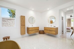 Une salle de bain moderne avec deux meubles-lavabos en bois, des miroirs ronds et une grande fenêtre.