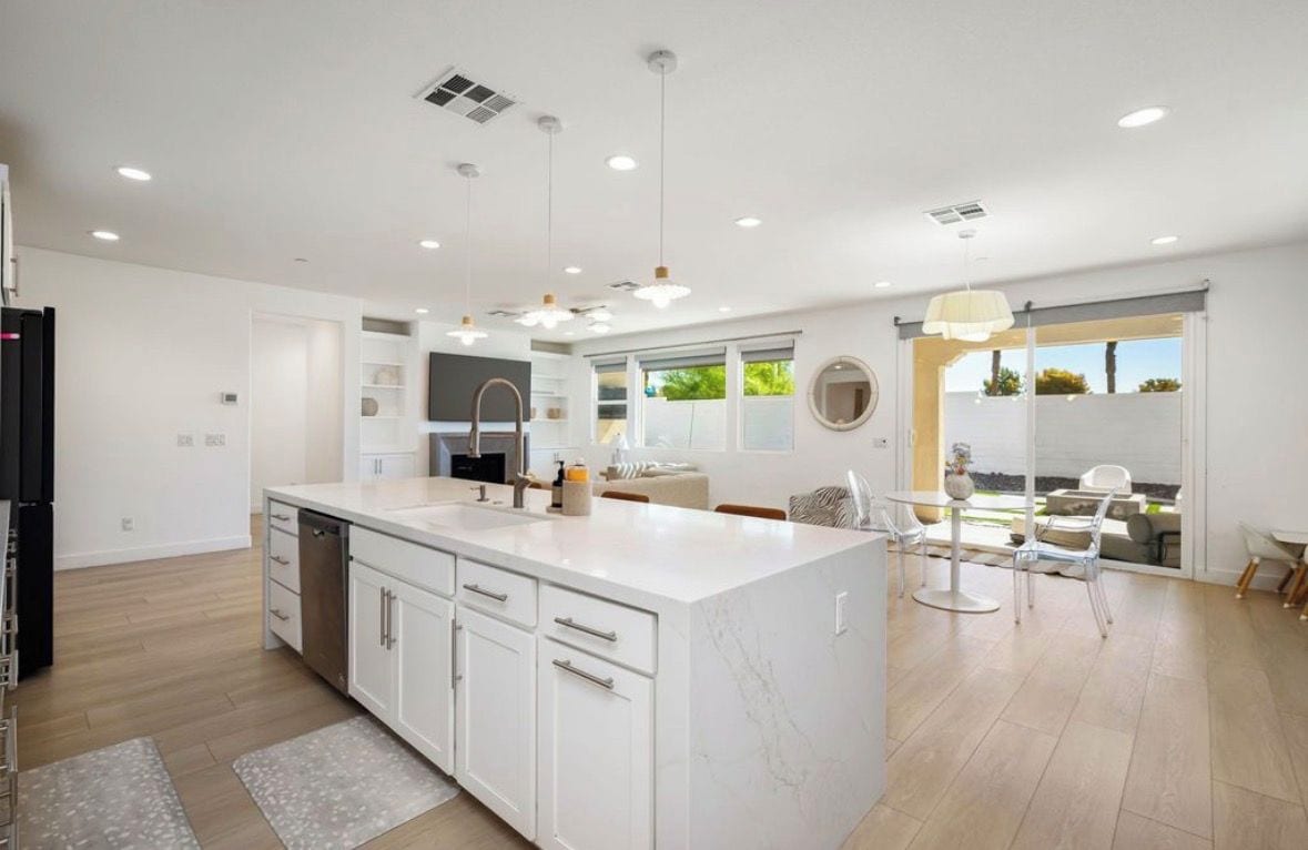 Une cuisine moderne avec des meubles blancs, un grand îlot central et des luminaires suspendus.