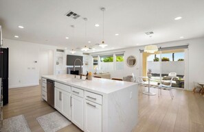 Une cuisine moderne avec des meubles blancs, un grand îlot central et des luminaires suspendus.