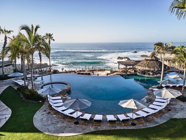 Ein Hotelpool mit Blick aufs Meer, umgeben von Palmen und Liegestühlen.