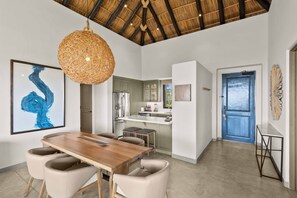Una cocina moderna con armarios blancos, un refrigerador de acero inoxidable y un comedor con mesa y sillas de madera.