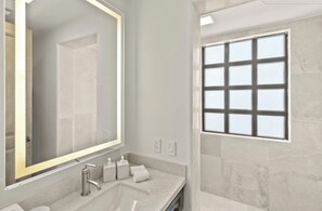 Ein modernes Badezimmer mit einem großen Spiegel, einem Waschbecken und einem Fenster.