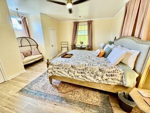A bedroom with a bed, a bedside table, a chair, a window with curtains, and a ceiling fan. - Solost SOMA Little Rock (Little Rock)