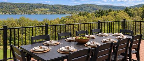 Una terraza con una mesa preparada para seis personas, con vistas a un lago y colinas.
