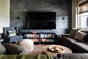 Una sala de estar con un televisor de pantalla plana montado en una pared de ladrillo, una estantería llena de libros, un sofá y una mesa de centro.