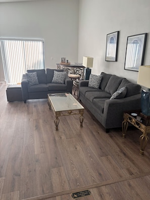 A living room with two sofas, a glass coffee table, and a wooden floor. - Spacious 4-bedroom house in beautiful Kissimmee (Kissimmee)