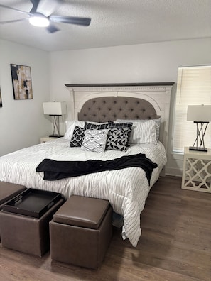 A bedroom with a bed, two nightstands, a ceiling fan, a window with blinds, and a wall-mounted artwork. - Spacious 4-bedroom house in beautiful Kissimmee (Kissimmee)