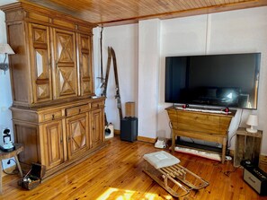 Een kamer met een houten kast, een televisie, een houten bankje en een tafeltje met een lamp.