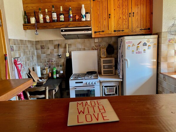 Een keuken met houten kastjes, een fornuis, een koelkast en een aanrecht met een bord waarop staat 'MADE WITH LOVE'.