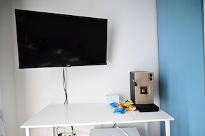 A white desk with a flat-screen TV mounted on the wall, a beige computer tower, and some snack packets on the desk. - Casa Marina—Room with a Sea View (Sicilia)