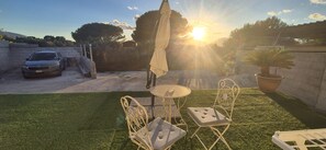 Eine Terrasse mit Tisch und Stühlen, ein Auto und ein Gebäude im Hintergrund.