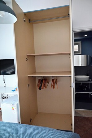 A room with a bed, a wardrobe with hanging clothes, a desk with a computer, and a bathroom with a sink. - Casa Marina—Room with a Sea View (Sicilia)