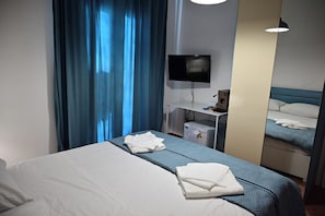 A hotel room with a bed, a television, a desk, and a mirror. - Casa Marina—Room with a Sea View (Sicilia)
