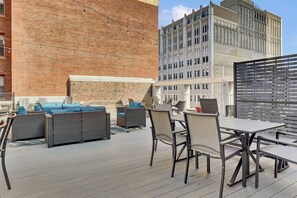 An outdoor patio with wicker furniture and a table, set against a brick wall and a modern building. - PremiumStays: 2 bd loft w/balcony : Playhouse sq : Theater : Arena : Parking (Cleveland)