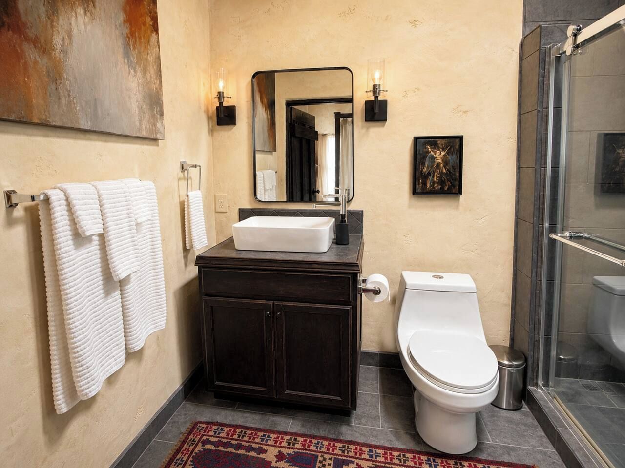 Une salle de bain avec un meuble-lavabo en bois foncé, un lavabo blanc, des toilettes et un espace douche.