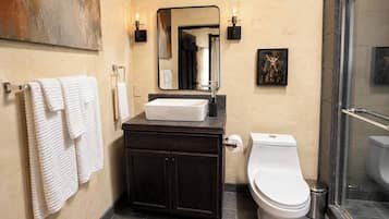 Une salle de bain avec un meuble-lavabo en bois foncé, un lavabo blanc, des toilettes et un espace douche.