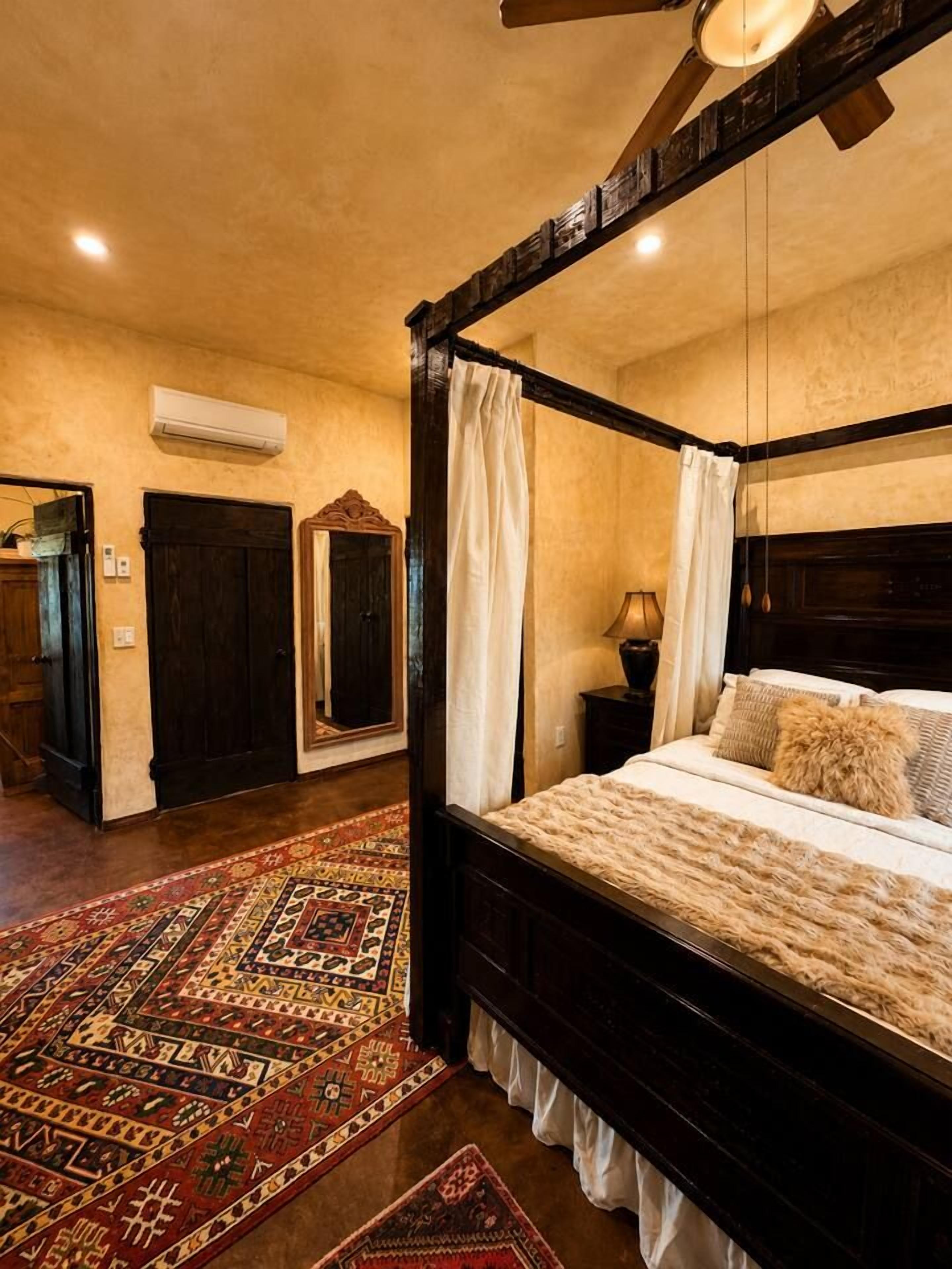 A four-poster bed with a canopy, a patterned rug, and a ceiling fan.