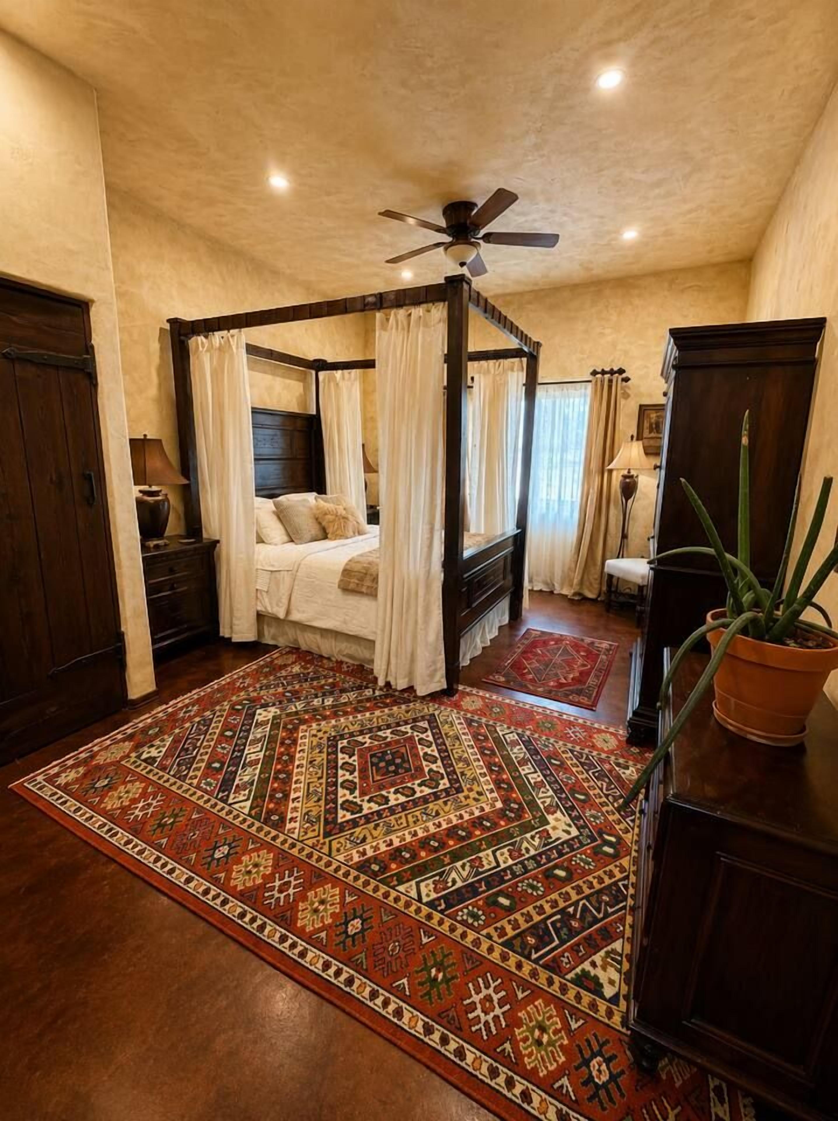 Un lit à baldaquin, un grand tapis à motifs et un ventilateur de plafond.