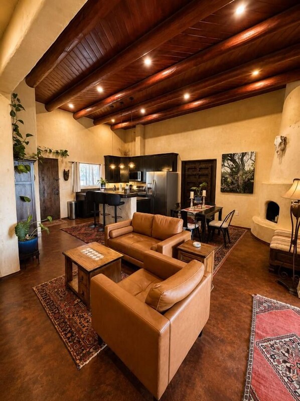 A spacious living area with a brown leather sofa, a wooden coffee table, and a kitchen in the background.
