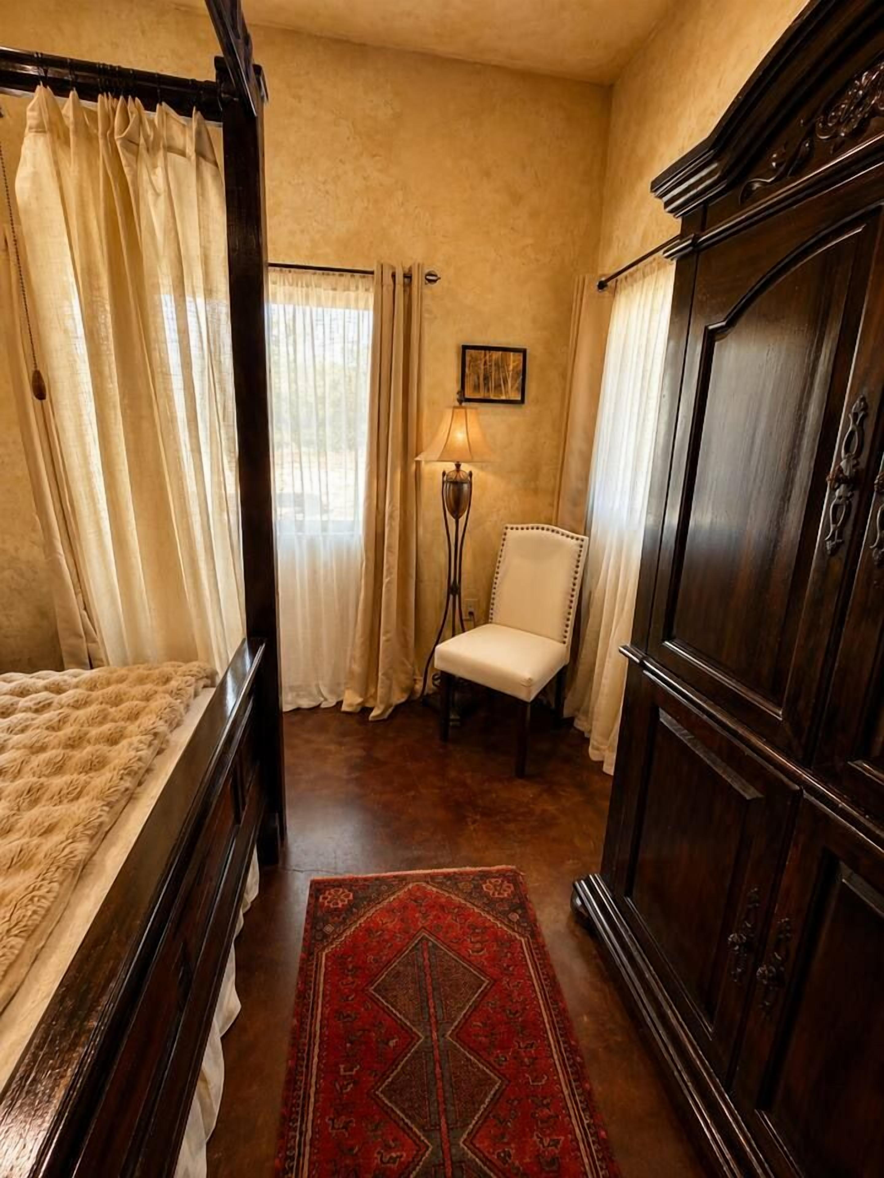 Ein Schlafzimmer mit einem Himmelbett, einem Sessel, einem Kleiderschrank und einer Stehlampe.