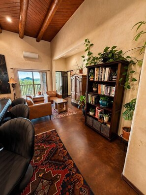 A spacious living room with a fireplace, leather sofas, a coffee table, and a bookshelf filled with books and plants.